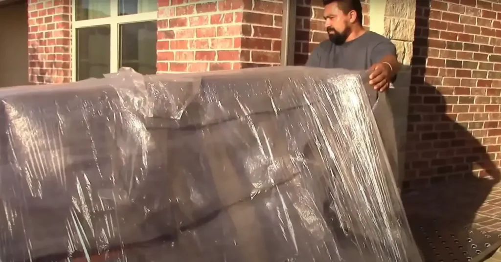Local Movers 14 Mover lifting a plastic-wrapped sofa outside a brick house
